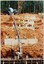 At the top of the photo is a concrete truck with a long funnel set up from the truck down the steep slope to deliver concrete to the place where there are two workers at the bottom of the photo - as part of the rebuilding of the Puffing Billy line to Gembrook.