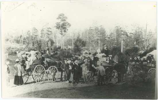 Black and white photograph depicting people and horses in the foreground and trees in the background.