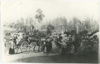 Black and white photograph depicting people and horses in the foreground and trees in the background.