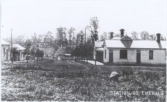 Black and white photograph depicting an intersection with shops on either side.