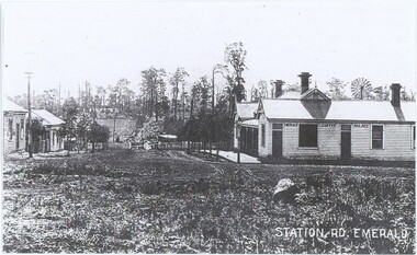Black and white photograph depicting an intersection with shops on either side.