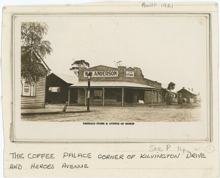 Black and white photograph depicting a store at a street corner, with printed text immediately below the photograph and handwritten text on the paper below.