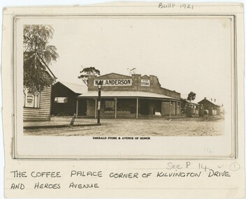 Black and white photograph depicting a store at a street corner, with printed text immediately below the photograph and handwritten text on the paper below.