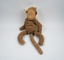 A brown toy monkey with a lighter brown felt face; the monkey's mouth is a red line and its eyes are closed.