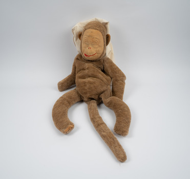 A brown toy monkey with a lighter brown felt face; the monkey's mouth is a red line and its eyes are closed.