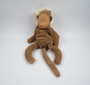 A brown toy monkey with a lighter brown felt face; the monkey's mouth is a red line and its eyes are closed.