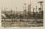 Black and white postcard depicting a field with houses and trees in the background.