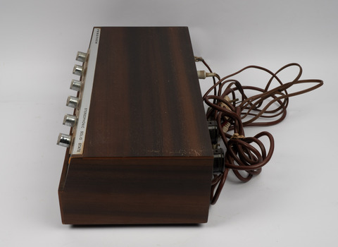Side view of amplifier showing row of control buttons along the front and electrical cords on the back.