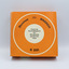 Bottom view of orange box containing rotary slide magazine with information in German in the centre.