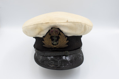 Black patent leather peak decorated with oak leaves, black chin strap, gold embroidered crown, ribbed white cotton top. 