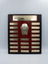 A wooden perpetual trophy plaque with brass plates and a brass netball hoop and ball in the center.