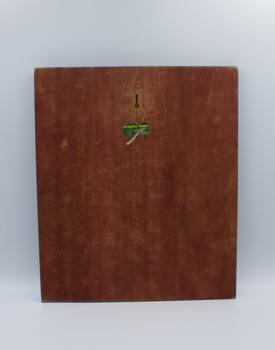 The wooden reverse of a trophy plaque, with a green sticker in the center-top. 