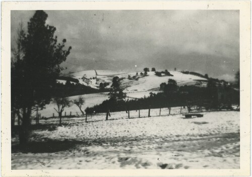 A black and white photograph of a field and hill covered in a layer of snow.