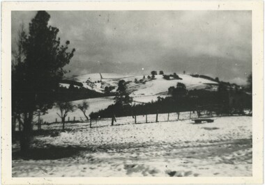 A black and white photograph of a field and hill covered in a layer of snow.