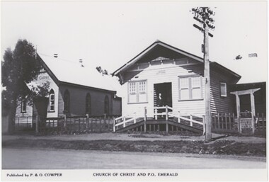 A black and white photograph featuring two buildings by a road, with publication and photograph details printed below.