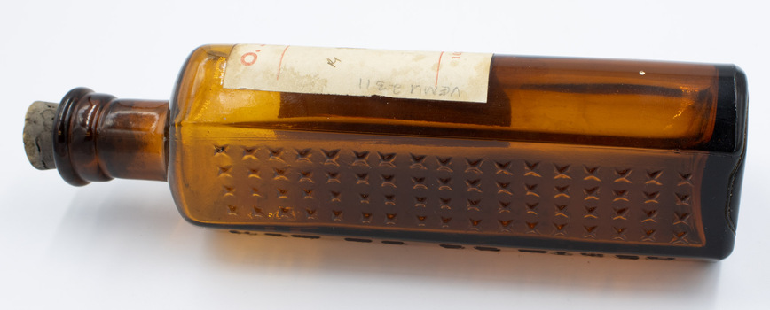 Side view of poison bottle with stopper lying flat on back.