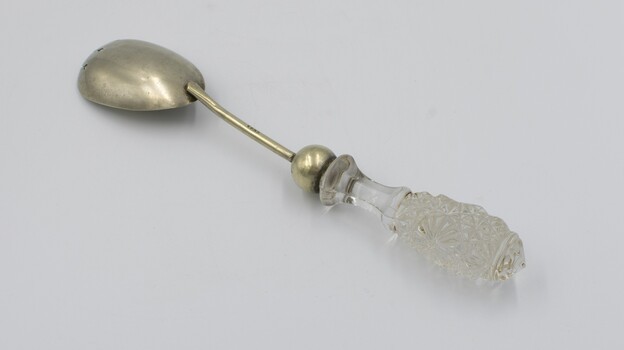 Salad serving fork in prone position with glass handle in foreground.
