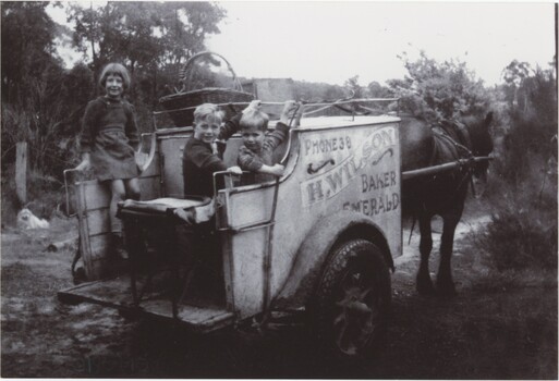 A black and white photograph of three children on the back of a horsecart.