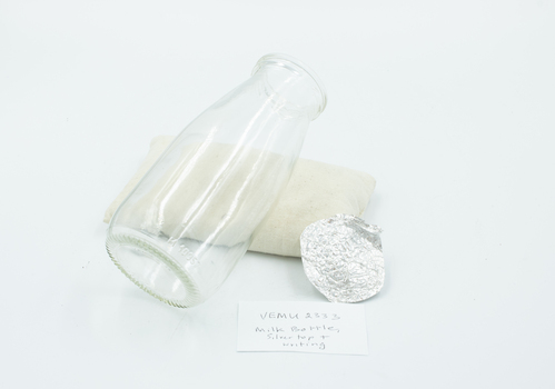 Small milk bottle with separate pressed metal lid and note.