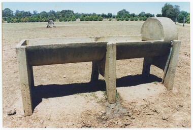A printed colour photograph depicting a concrete trough from side-on, with a pipe going into the higher right side.