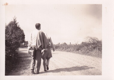 A male and female hiker walking along a country road. The male is carrying a billy.