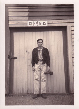 Young man in hiking clothes standing in front of 'Clematis' sign, holding a shoe.