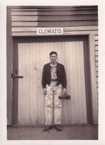 Young man in hiking clothes standing in front of 'Clematis' sign, holding a shoe.
