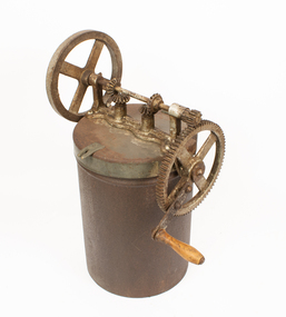 A rusted cylindrical metal container with gears and a handle on the lid.