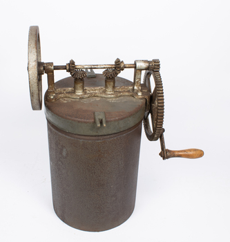 A rusted cylindrical metal container with gears and a handle on the lid.