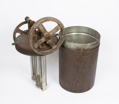 A rusted metal container and a lid with gears and a whisk-like structure reaching downwards.