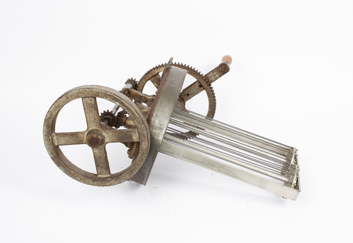 A metal lid with gears, a handle, and a whisk-like structure reaching downwards.