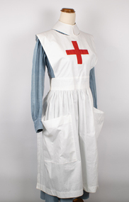 Nurse apron with red cross on bib and two large pockets on skirt.