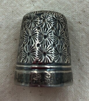 Silver thimble with dense floral design on side and wide band around rim.