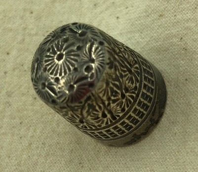 Top of silver thimble showing single daisy-type flower decoration.
