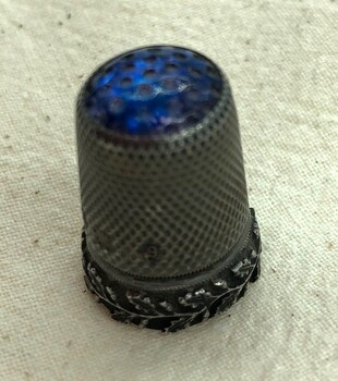 Decorative silver thimble with blue glass top prominent.