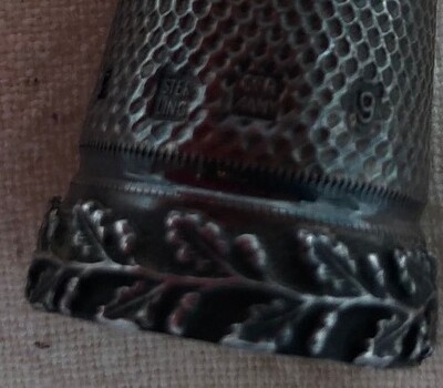 Rim of decorative silver thimble with manufacturers imprint visible on the lower part of the side.