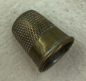 Brass thimble with honeycomb pattern on side and wide plain band around the turned-up rim.
