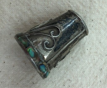 Silver thimble with scroll decoration on the side and abalone inset on band on rim. Seam on side visible.