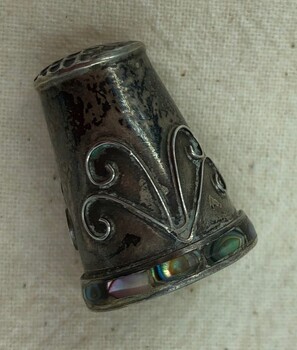 Closer view of thimble featuring scroll design on the side and abalone inset on band on rim.
