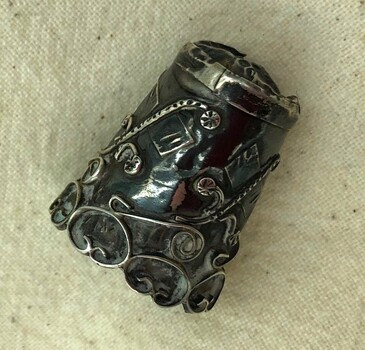 Ornate silver thimble showing decorative applied scrollwork.