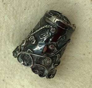 Ornate silver thimble showing decorative applied scrollwork.