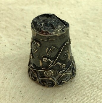 Top of ornate silver thimble showing damage and solder repairs.