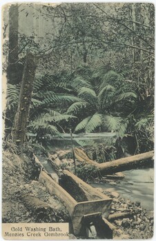 A hand-coloured postcard depicting a creek surrounded by trees and shrubs, with a gold-washing bath in the foreground and a printed caption in the bottom-left.