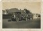 A sepia photograph of a truck pulling trailers with two large logs down a street with homes.