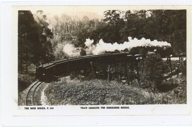 A photocopy of a black and white postcard of a steam train crossing a curving wooden trestle bridge.