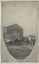 A black and white oval-shaped photograph of a yard with tools, wagons, and a wooden shed.