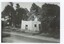 A black and white photograph of a brick or stone and wood building by a road.