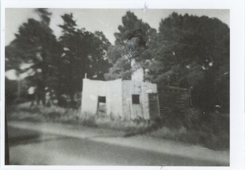 A black and white photograph of a brick or stone and wood building by a road.