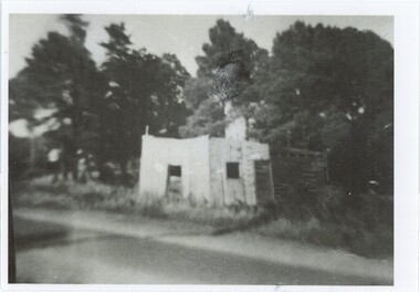 A black and white photograph of a brick or stone and wood building by a road.