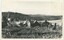 A black-and-white photograph of a house in a field, with hills in the background.